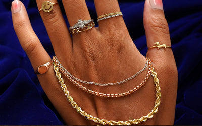 The back of a models hand wearing several Automic Gold rings with three different solid gold chains wrapped around their palm