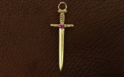 A yellow gold ruby Sword Charm resting on the back of a model's hand