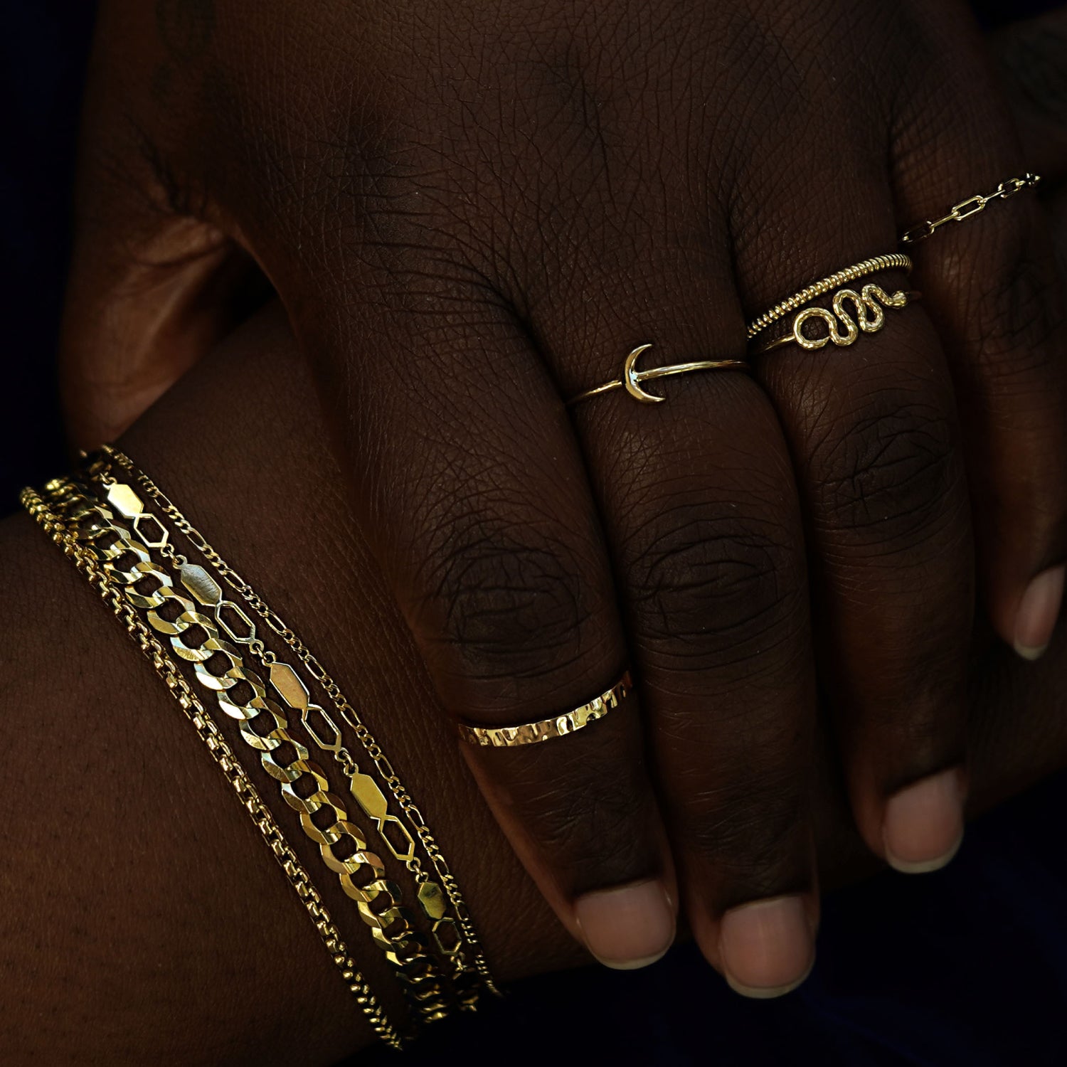 A model posing with one hand covering the other wearing several Automic Gold rings and bracelets