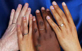 Close up view of four different model's hands of varying skin tones wearing Automic Gold wedding bands of various widths