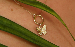 Three plant leaves artfully draped over a model's neck wearing a 14k yellow gold Lockless Cable Chain with a Butterfly Charm