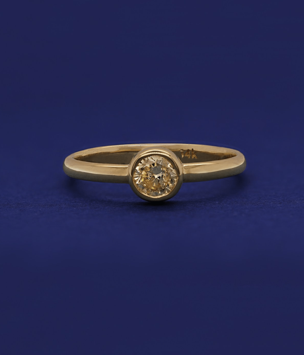 A 14k yellow gold bezel set 1/3ct Diamond Ring on a blue background