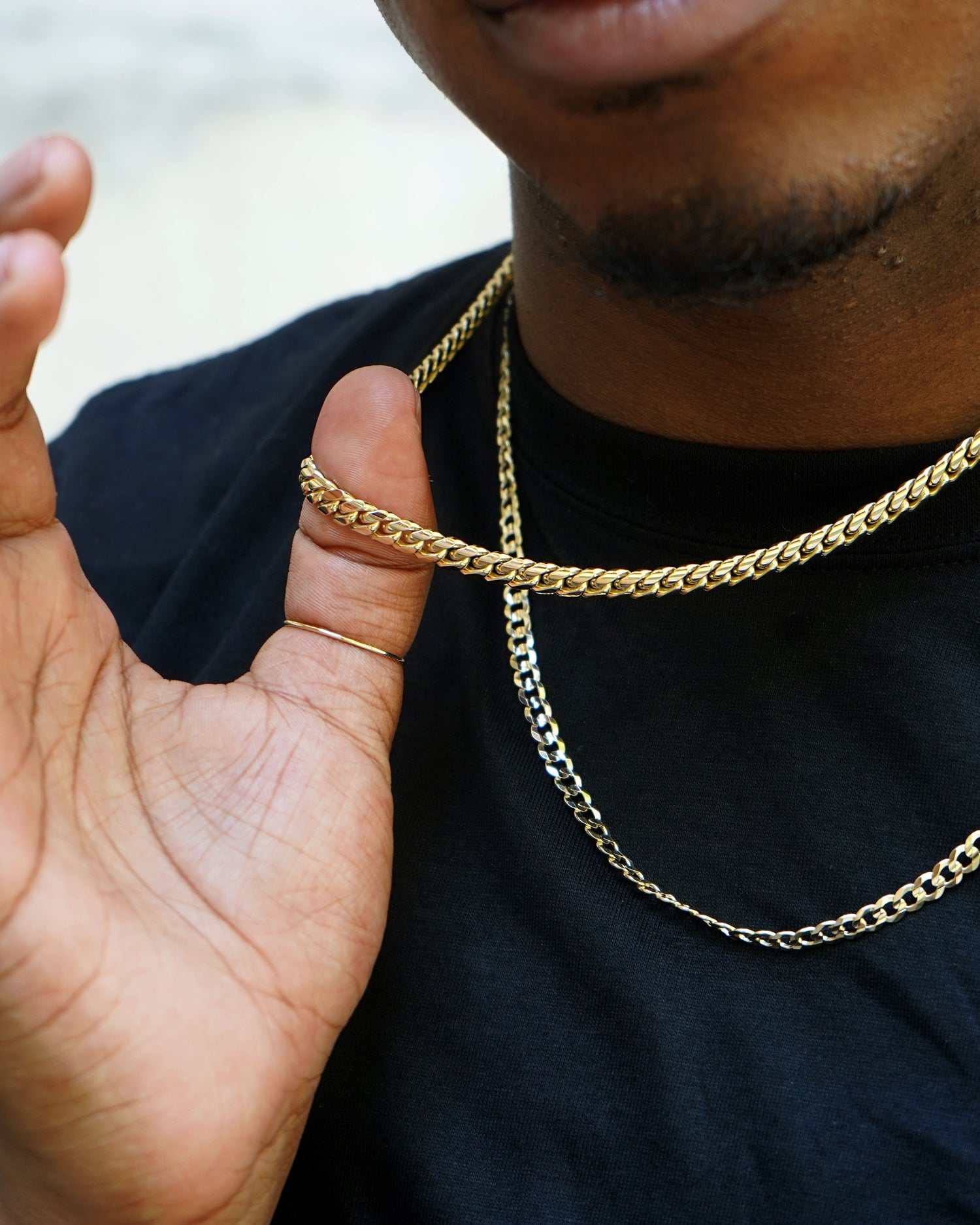 A model in a black shirt wearing two chunky solid gold chains is holding one up by their thumb which has a Line Ring on it