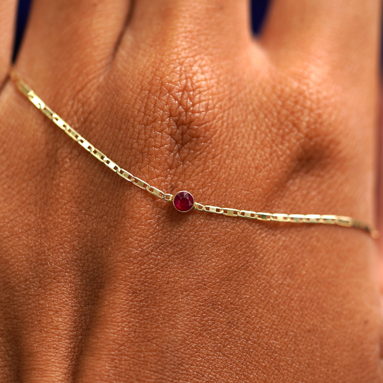 A solid gold Ruby Bracelet resting on the back of a model's hand