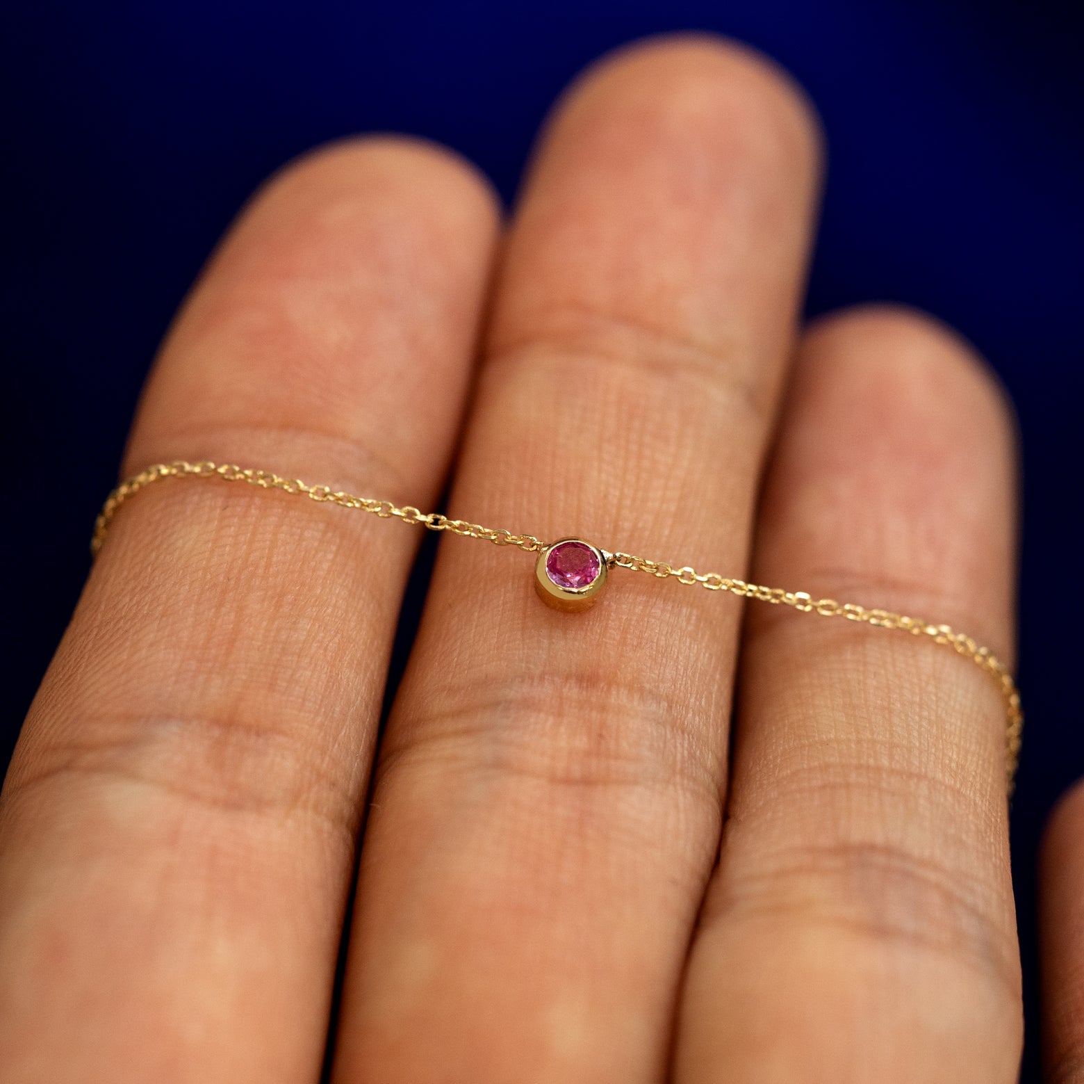 A pink sapphire bezel set gemstone necklace laying over a models fingers to show the details of the setting