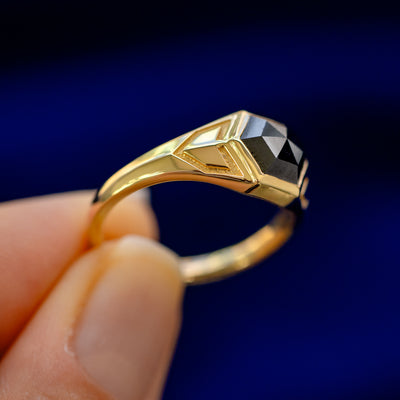 A model holding a 14k gold Transformation Ring sideways to show the details of the bezel setting and the stone