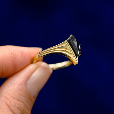 A model holding a 14k gold Journey Ring sideways between two fingers to show the details of the bezel setting and the stone
