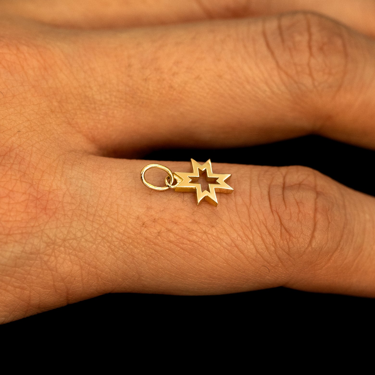 A 14k yellow gold Large Open 8 Pointed Star Charm for chain balancing on the back of a model's finger