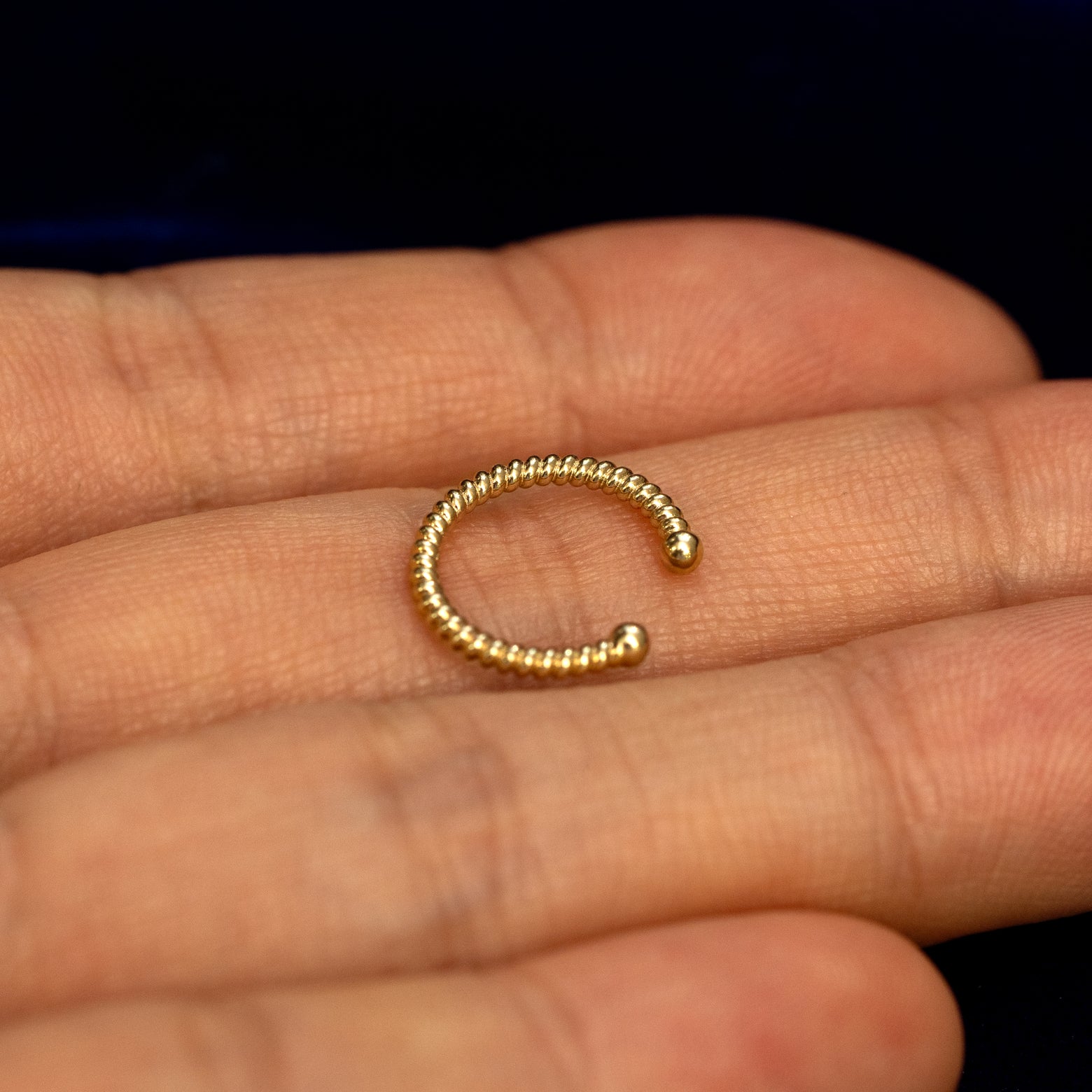 A solid 14 karat yellow gold Rope Cuff earring resting on a model's palm