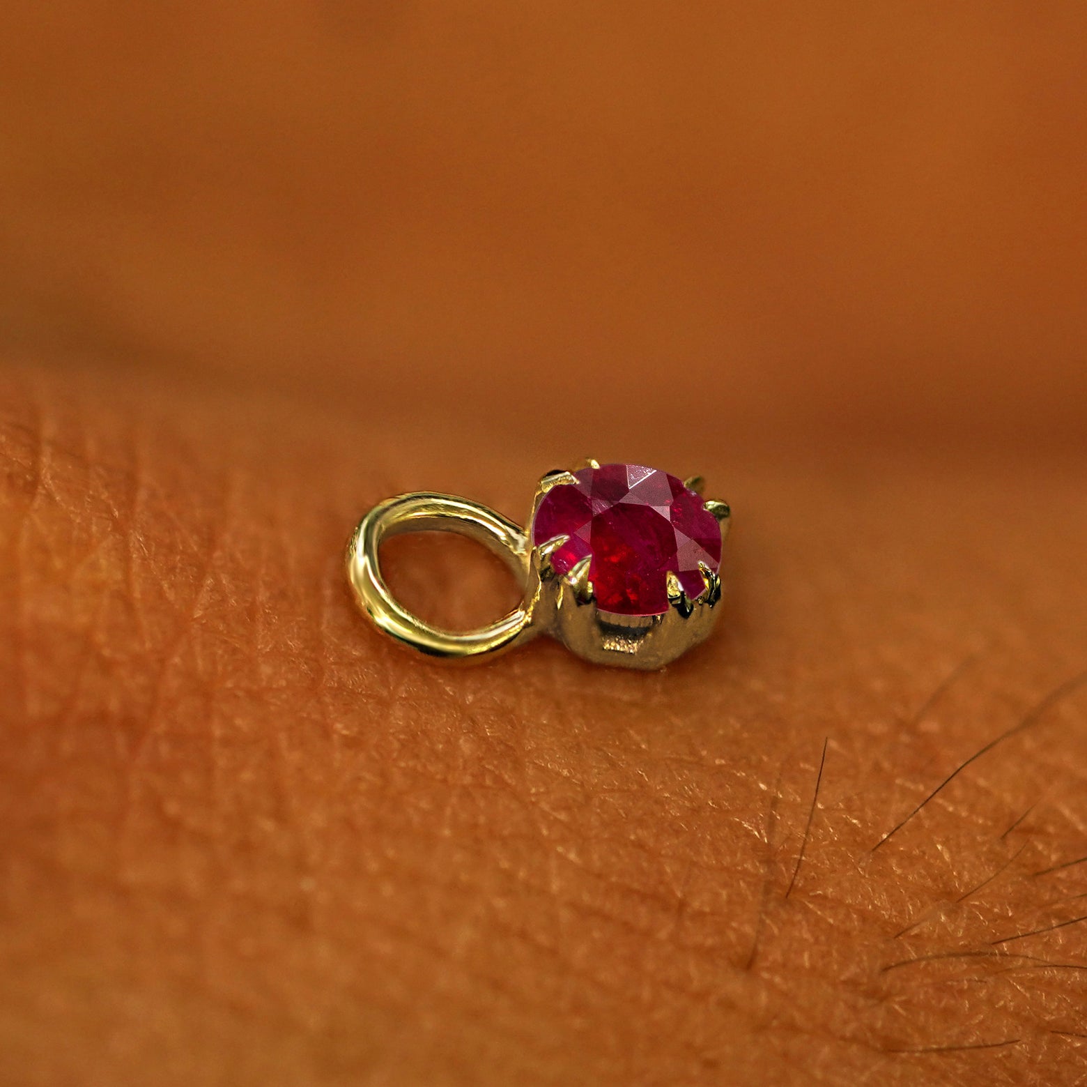 A solid yellow gold Ruby Charm for earring resting on the back of a model's hand