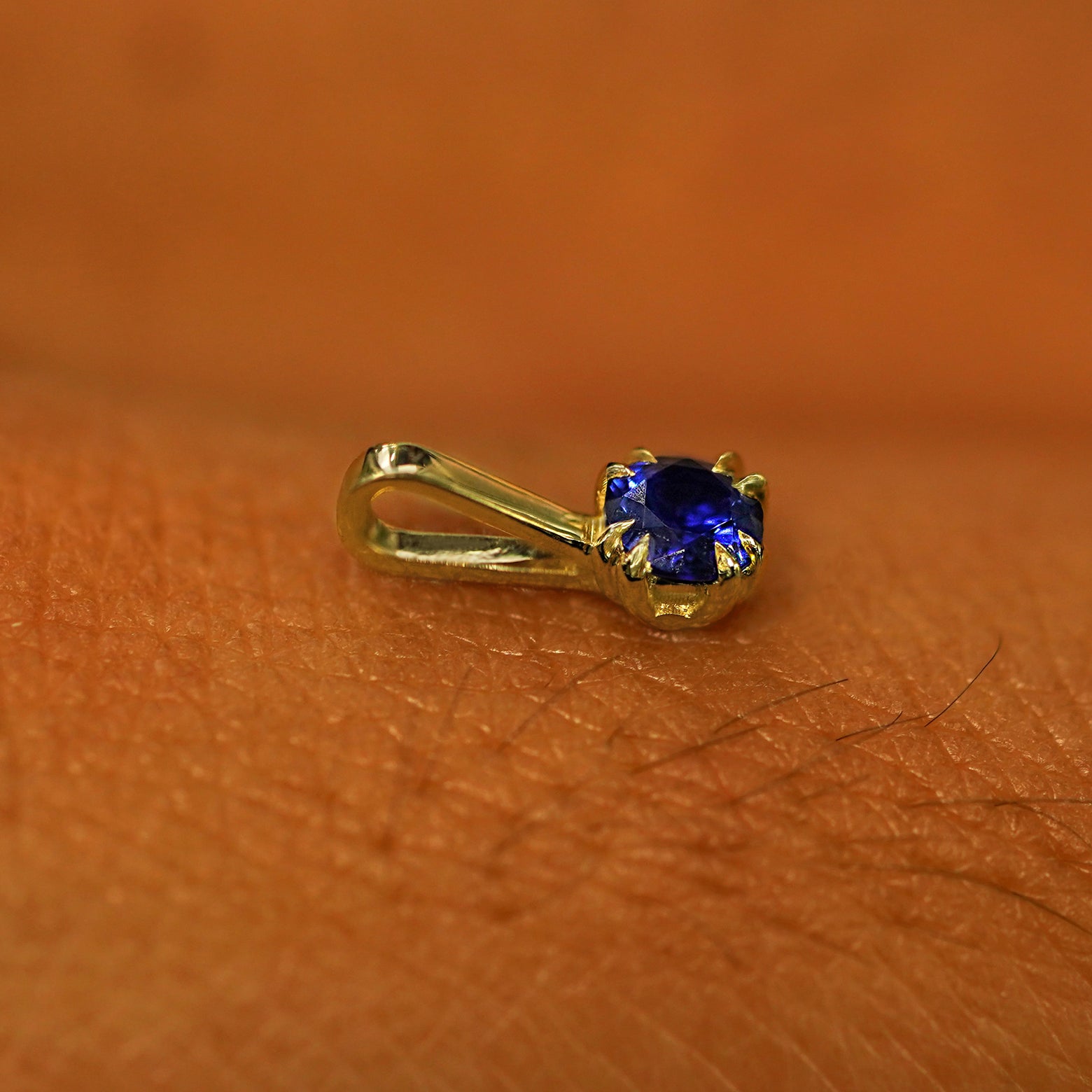 A 14k yellow gold Sapphire Charm for chain resting on the back of a model's hand
