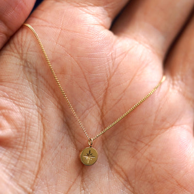 A solid yellow gold star disk necklace wrapped around a models hand
