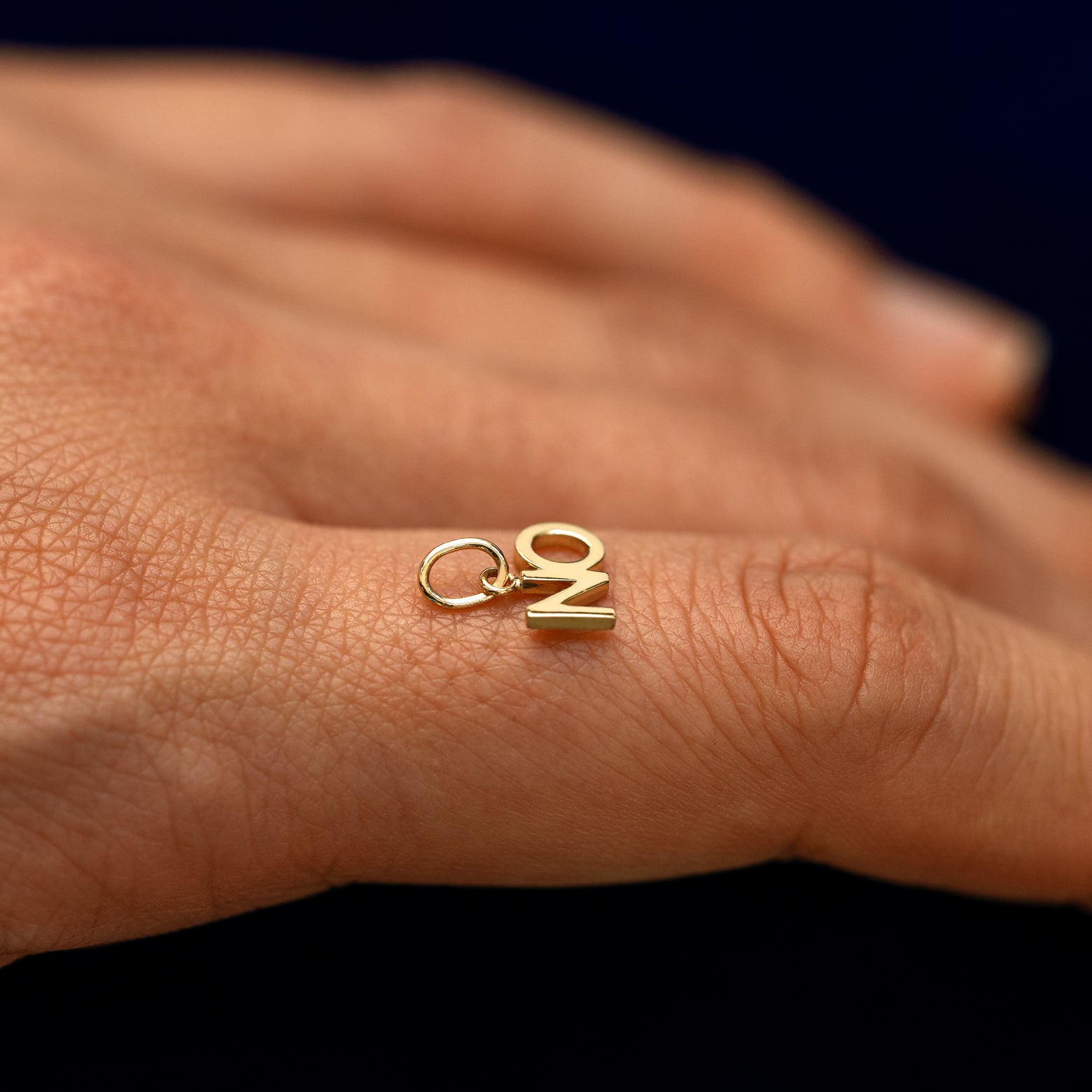 A solid 14k gold No charm resting on a models finger to show the bail details