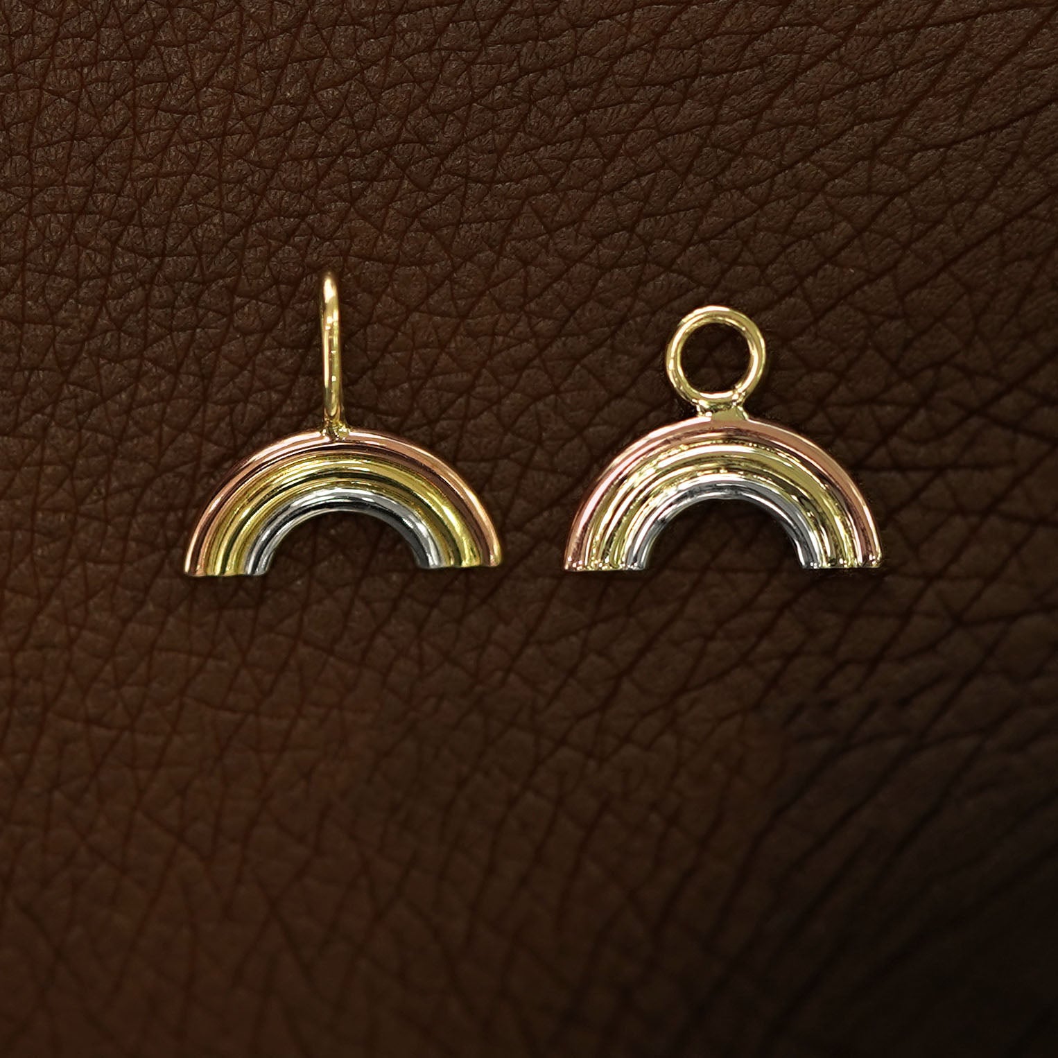 A solid 14k gold Rainbow Charm for earring and necklace laying on the back of a model's hand