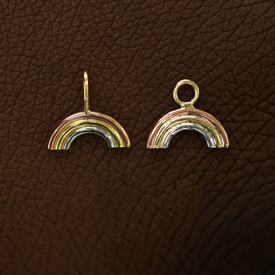 A solid 14k gold Rainbow Charm for earring and necklace laying on the back of a model's hand