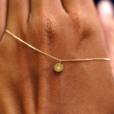 A solid yellow gold star disk necklace wrapped around the back of a models hand