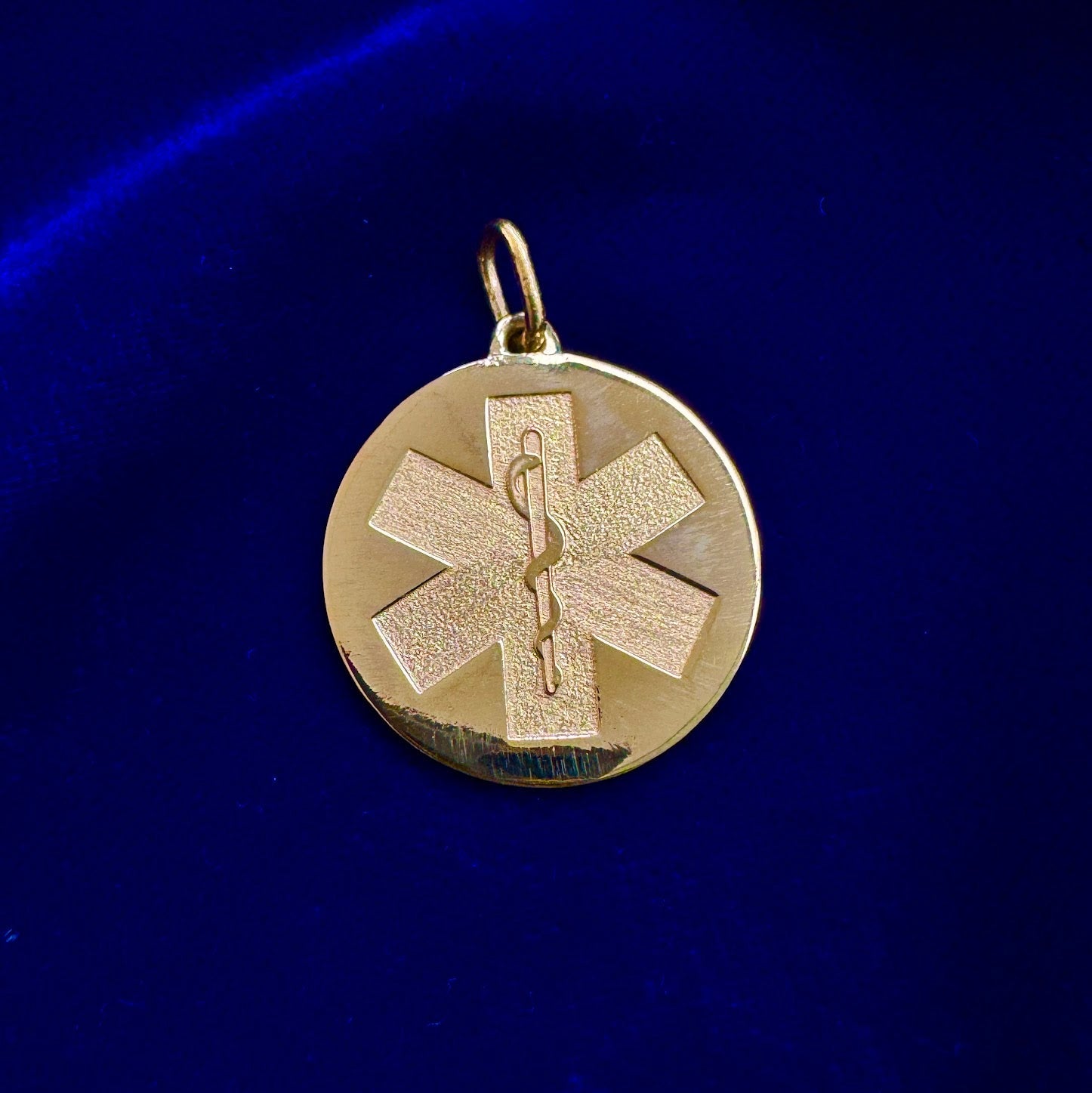 A solid 24k gold pendant with the medical alert symbol on a dark blue background