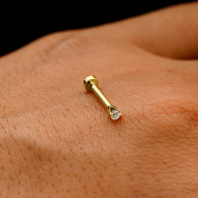 A solid 14k yellow gold 2mm Diamond Flatback Piercing resting on the back of a model's hand