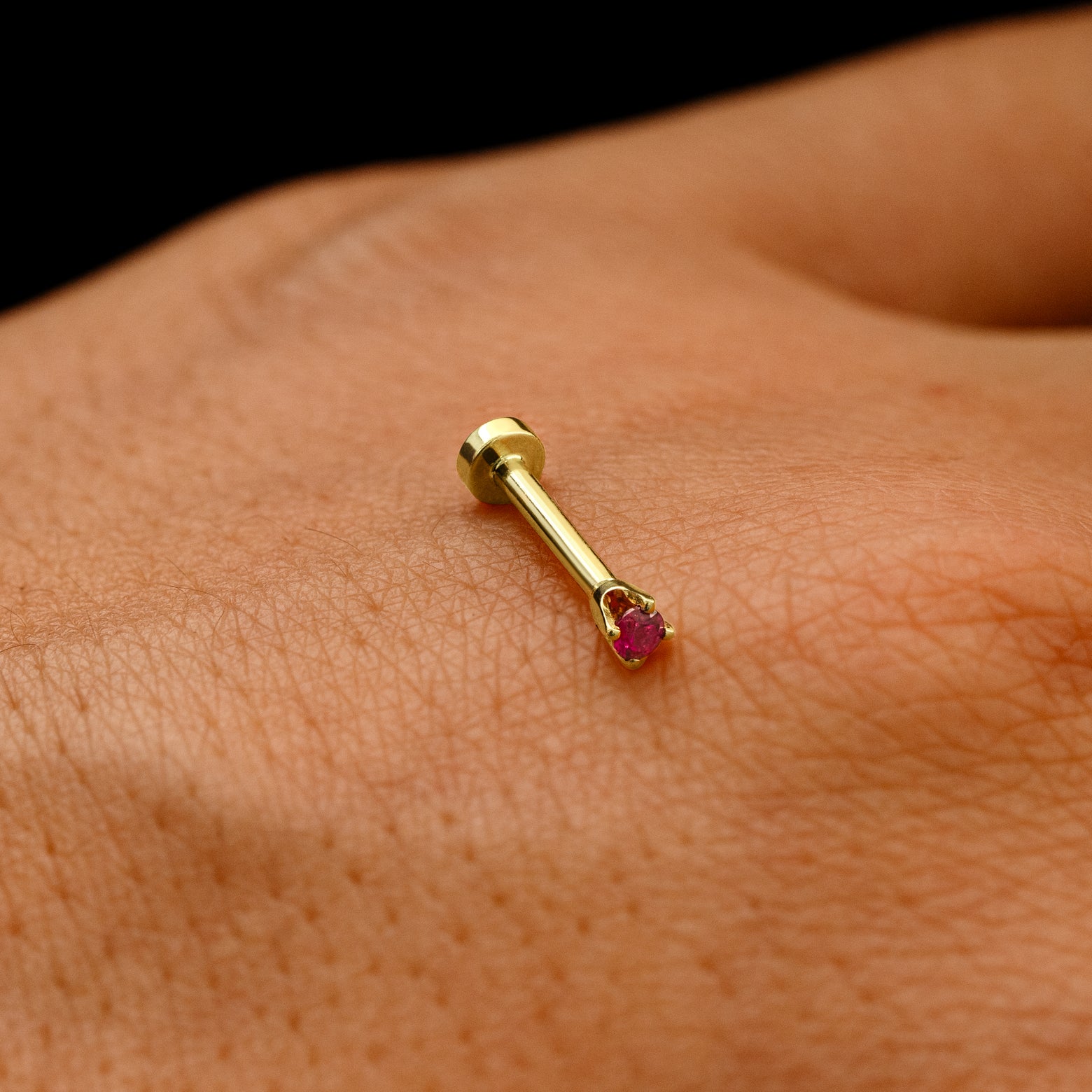 A solid 14k yellow gold 2mm Gemstone Flatback Piercing resting on the back of a model's hand