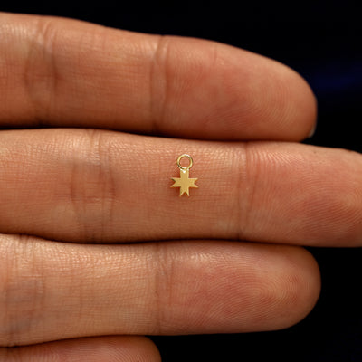 A solid gold 8 Pointed Star Charm for chain resting in a model's palm