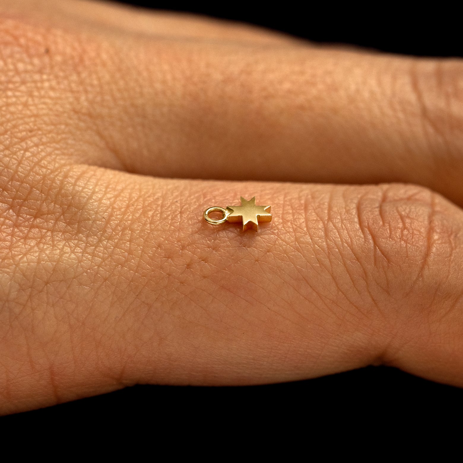 A 14k yellow gold 8 Pointed Star Charm for earring balancing on the back of a model's finger