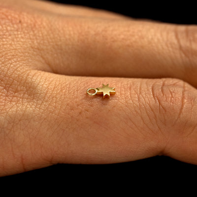 A 14k yellow gold 8 Pointed Star Charm for earring balancing on the back of a model's finger