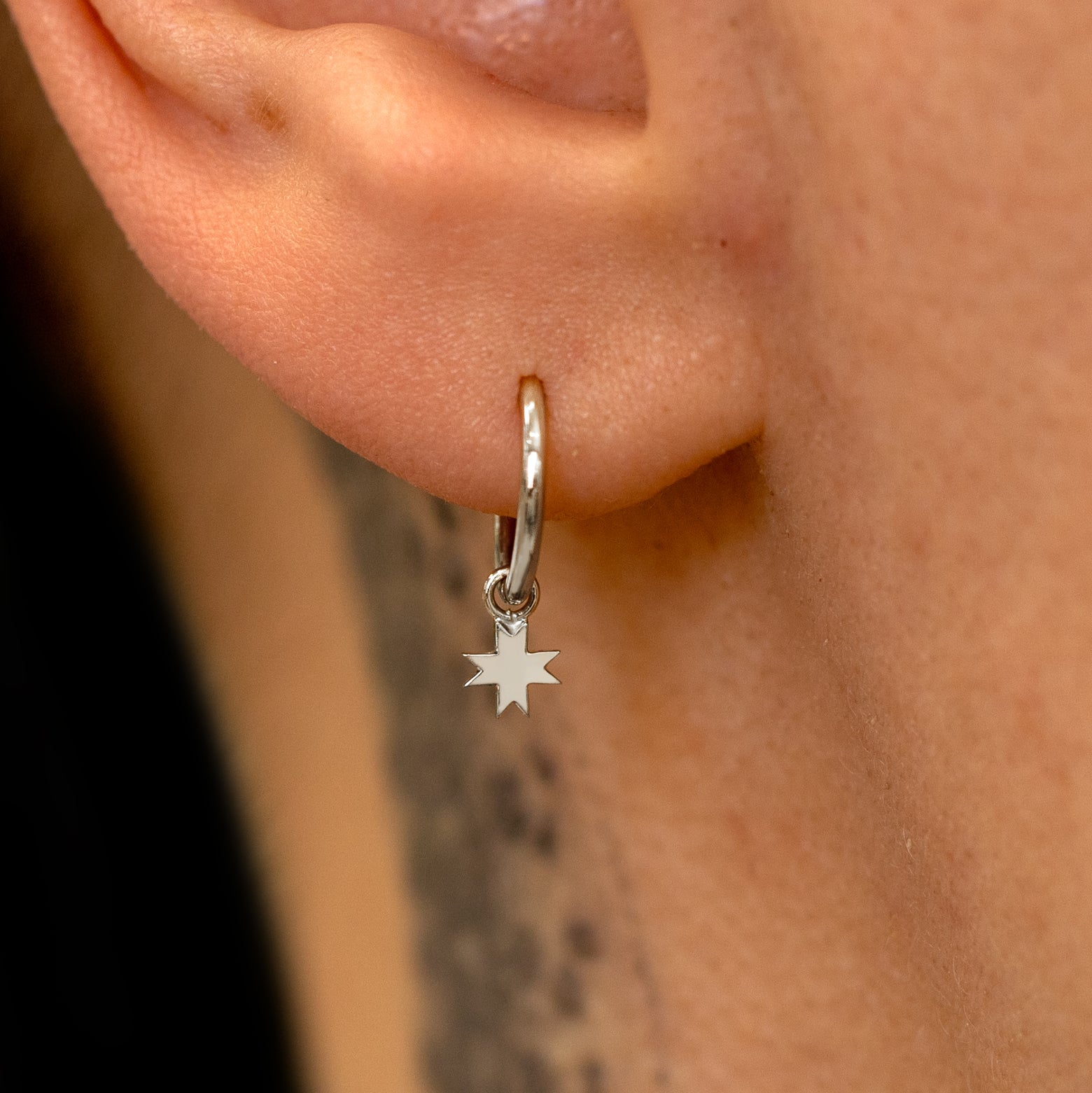 Close up view of a model's ear wearing a white gold 8 Pointed Star Charm on a Seamless Huggie Hoop