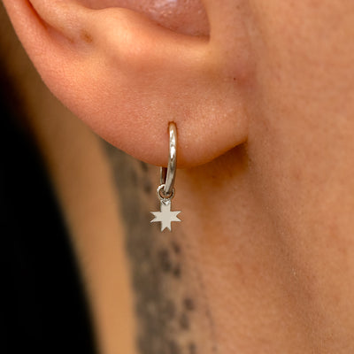 Close up view of a model's ear wearing a white gold 8 Pointed Star Charm on a Seamless Huggie Hoop