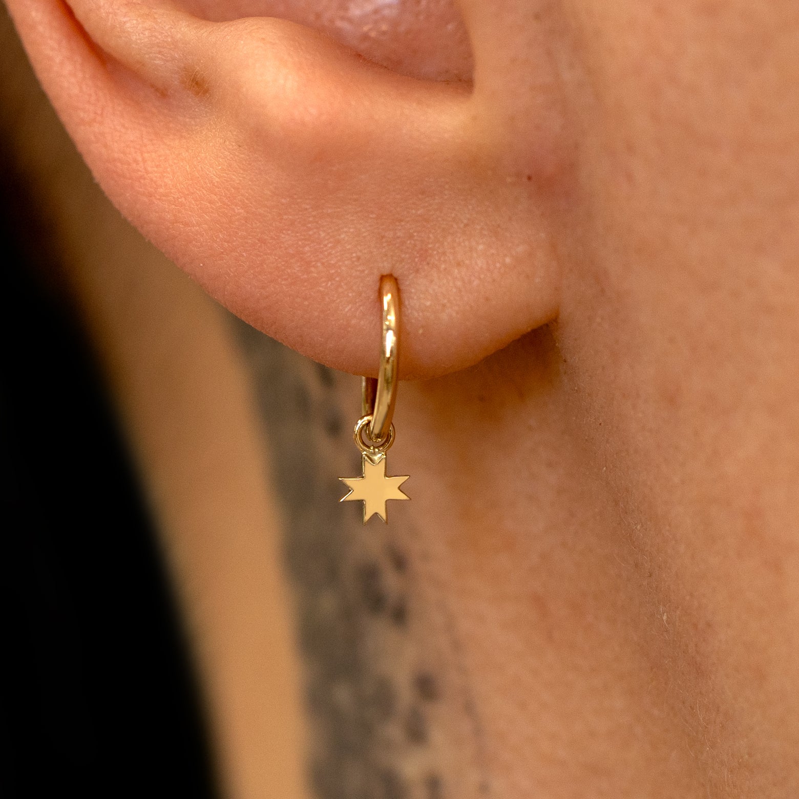 Close up view of a model's ear wearing a yellow gold 8 Pointed Star Charm on a Seamless Huggie Hoop