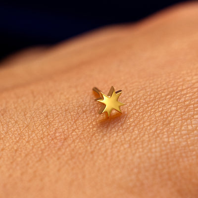 Close up view of the face of an 8 pointed star flatback piercing on the back of a models hand
