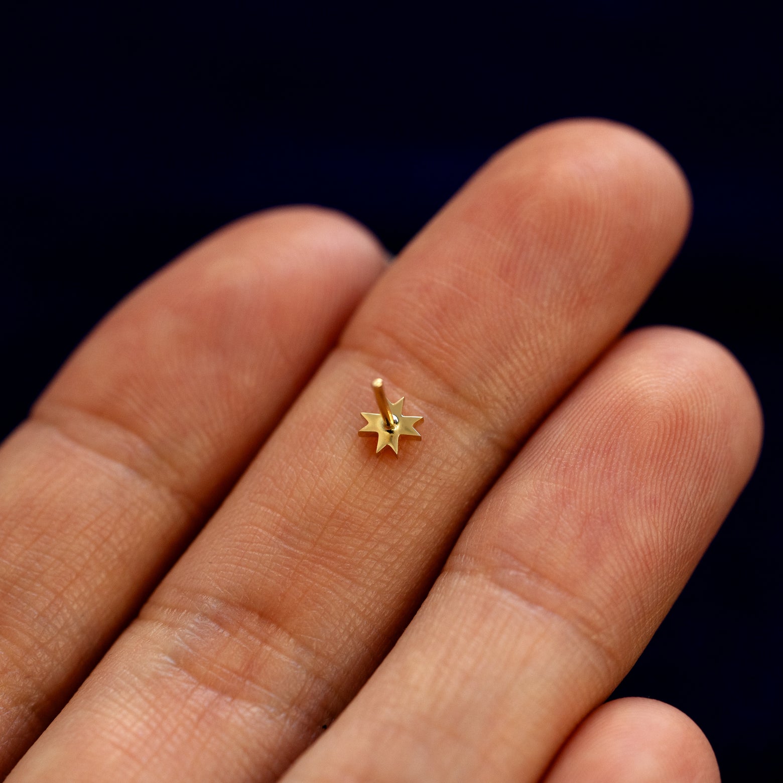 A model holding an 8 pointed star flatback piercing face down on their fingers to show details