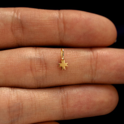 A solid gold 8 Pointed Star Charm for earring resting in a model's palm