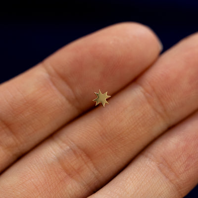 A model holding an 8 pointed star stud earring between two fingers to show the details