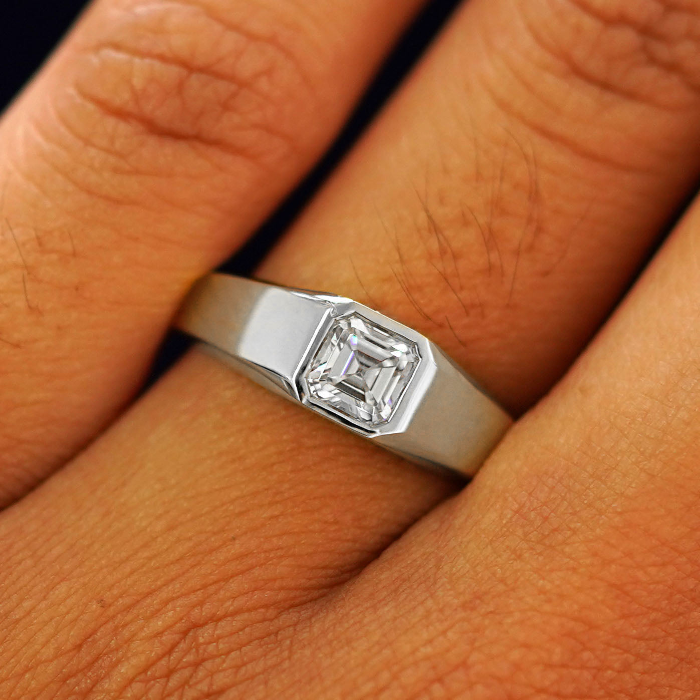 Close up view of a model's fingers wearing a platinum white lab moissanite Asscher Gemstone Signet Ring