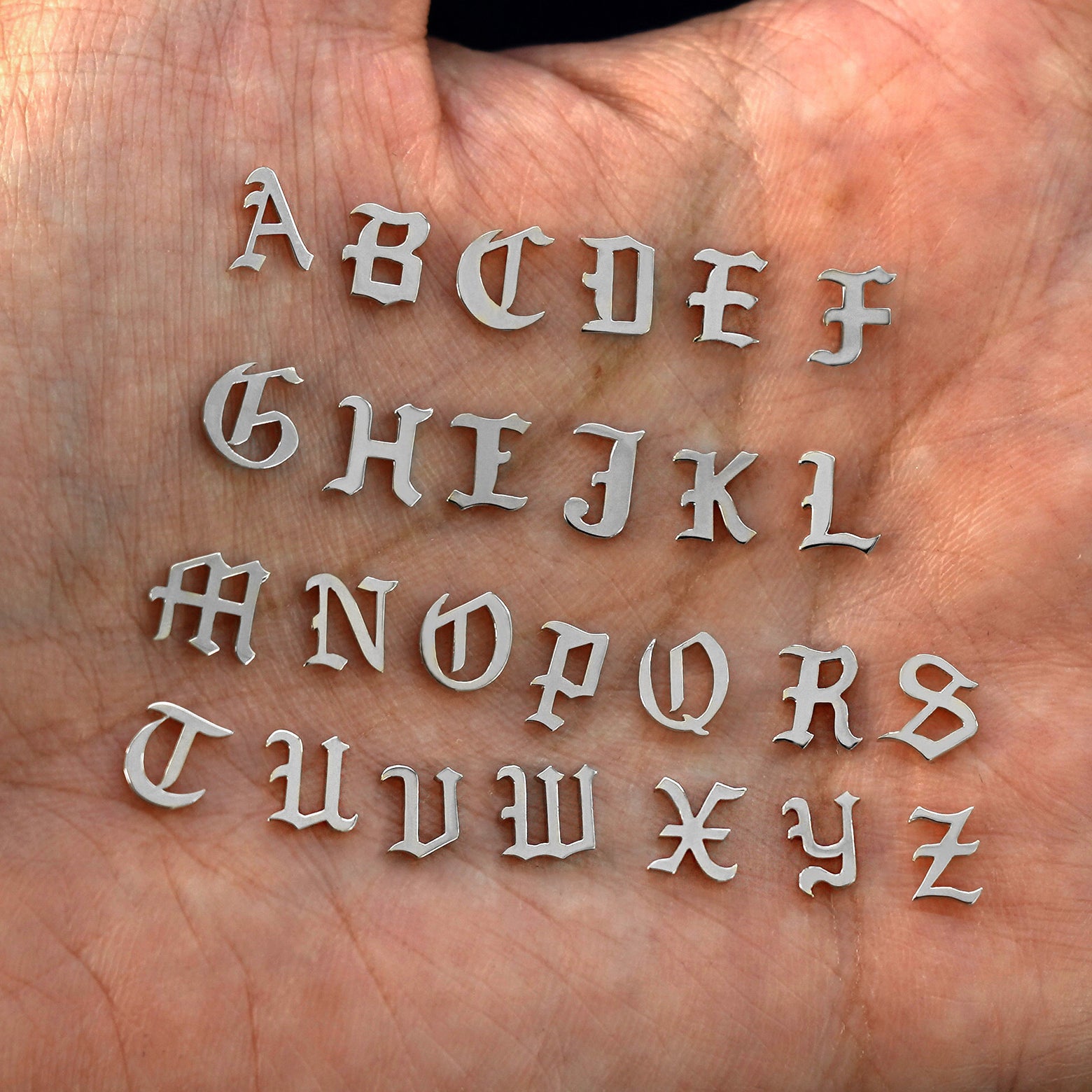 A model's palm holding solid 950 platinum versions of all 26 initials in the unique Automic Gold font