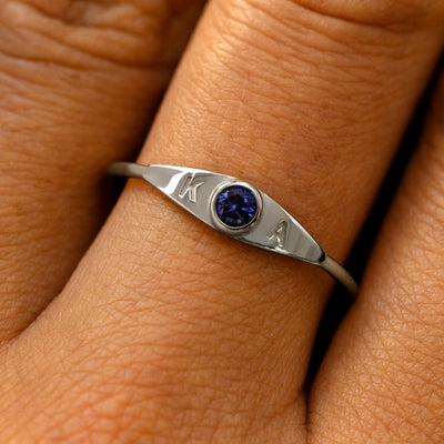 A model's finger wearing a 950 platinum sapphire gemstone monogram ring with the initials K A