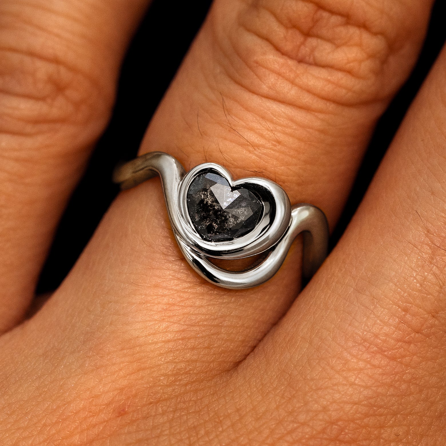 A model's hand wearing a 950 platinum Heart Salt and Pepper Diamond Infinite Wave Ring
