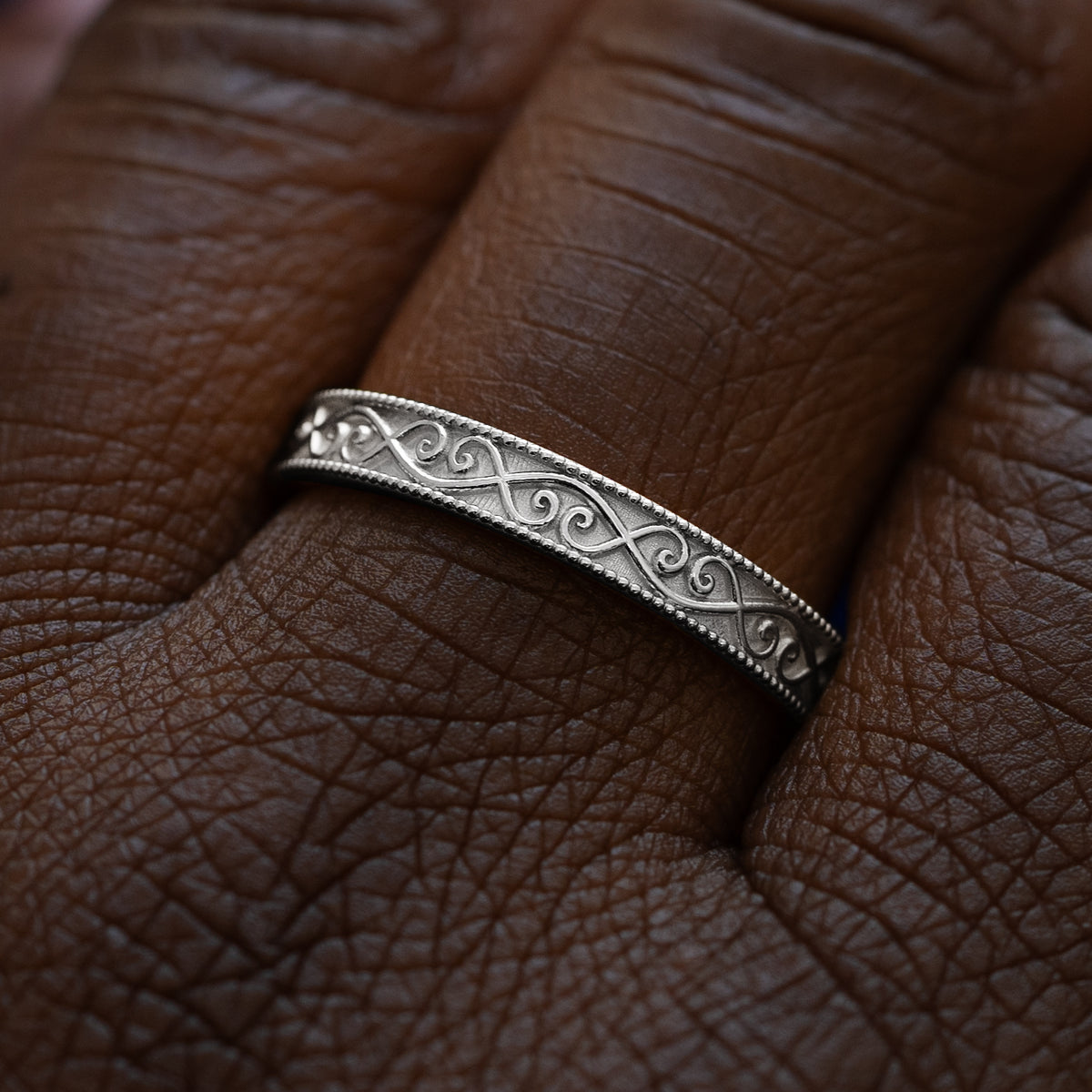 Close up view of a model wearing a solid 950 platinum milgrain scroll band