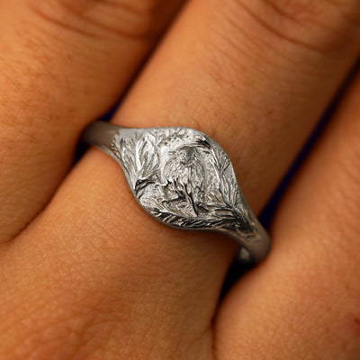 Close up view of a model's fingers wearing a 950 platinum Pine and Bird Signet Ring