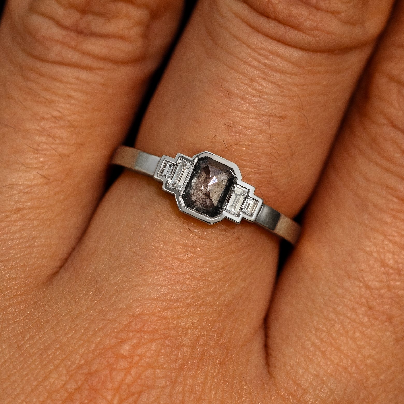 Close up view of a model's hand wearing a 950 platinum Emerald Cut Salt and Pepper and Clear Baguette Diamond Ring
