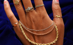 The back of a models hand wearing several Automic Gold rings with three different solid gold chains wrapped around their palm