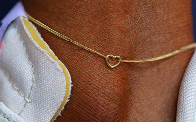 Close up view of a model's ankle wearing a yellow gold Heart Anklet