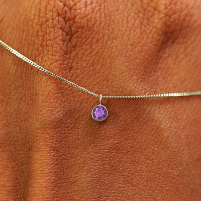 Close up view of a 14k champagne gold Amethyst Necklace draped across the back of a model's hand