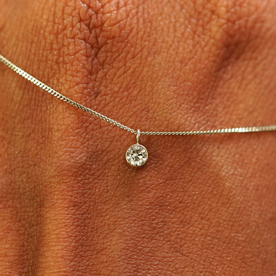 Close up view of a 14k champagne gold Champagne Diamond Necklace draped across the back of a model's hand