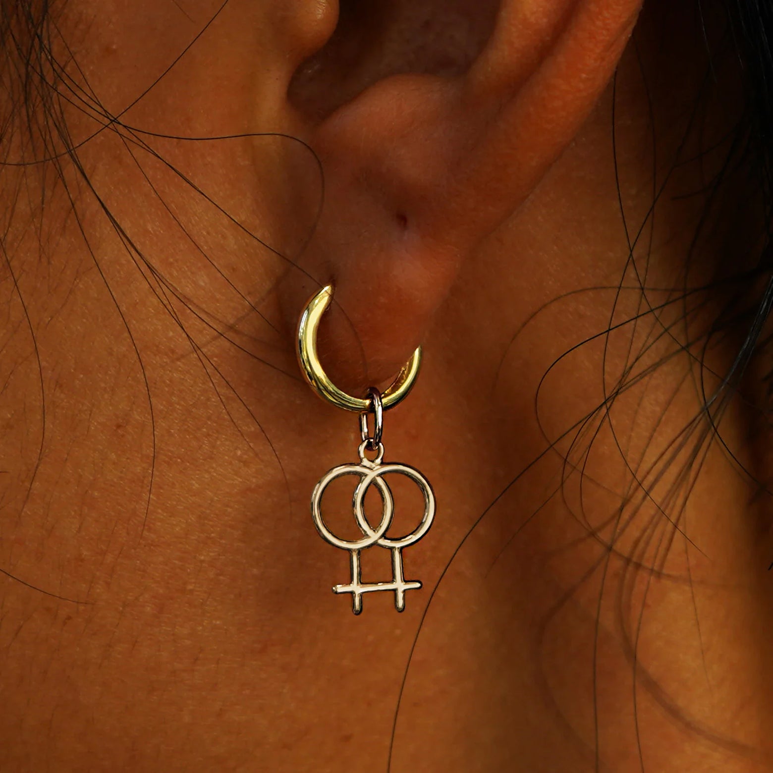Close up view of a model's ear wearing a champagne gold Lesbian Symbol Charm on a Curvy Huggie Hoop