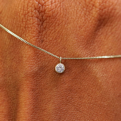 Close up view of a 14k champagne gold Moissanite Necklace draped across the back of a model's hand