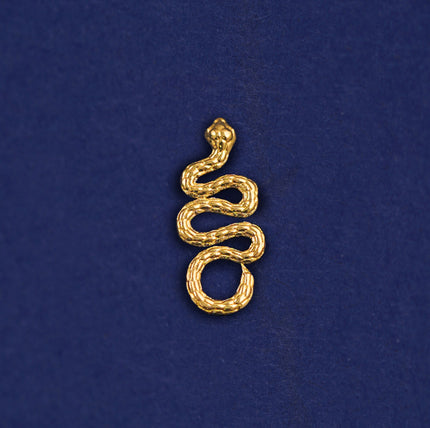 A 14k yellow gold Snake Charm on a dark blue background