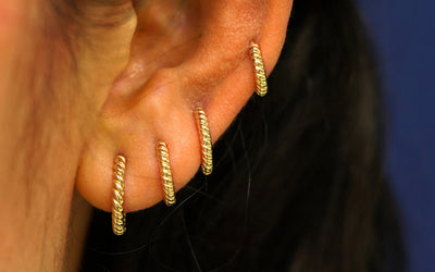 Close up view of a model's ear wearing four yellow gold rope huggies in four piercings