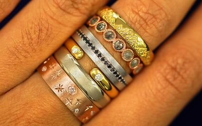 Close up view of a model's hand wearing several different Automic Gold wedding bands stacked on their finger