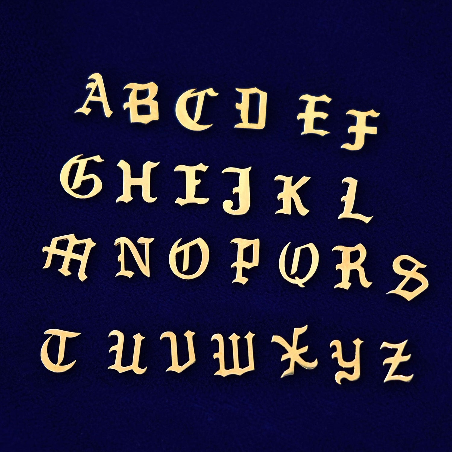 All 26 versions of the solid 14k yellow gold versions in the unique Automic Gold font lined up on a dark blue background